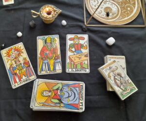 Tre carte dei Tarocchi disposte su un telo nero: L’Amore, Il Papa e Il Bagatto. Accanto, cristalli e mazzi di carte. Ambientazione spirituale e simbolica per una lettura intuitiva.